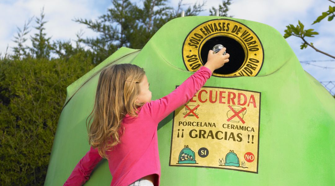 Una niña arroja un envase de vidrio en un iglú de reciclaje Una niña arroja un envase de vidrio en un iglú de reciclaje