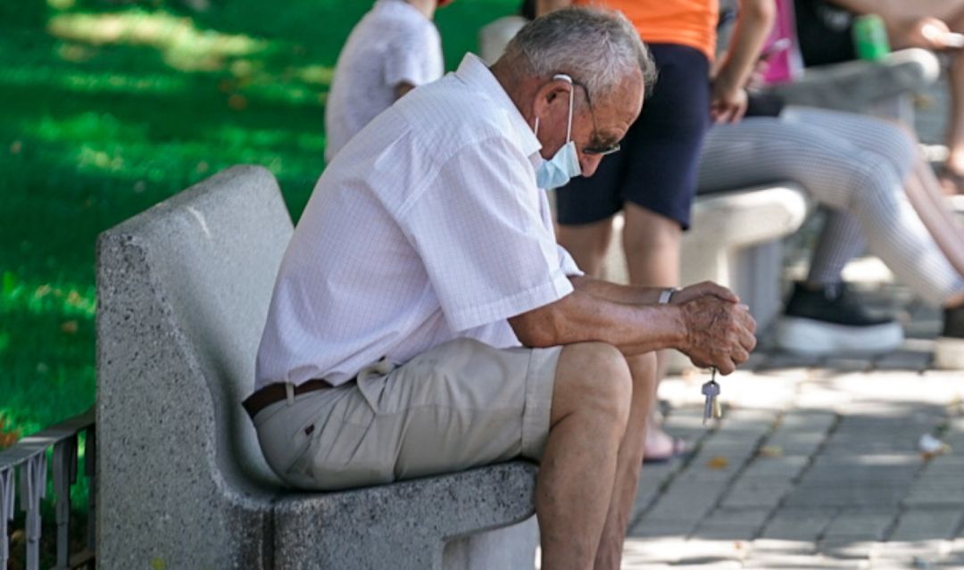 Un anciano con mascarilla sentado en un banco. Un anciano con mascarilla sentado en un banco.