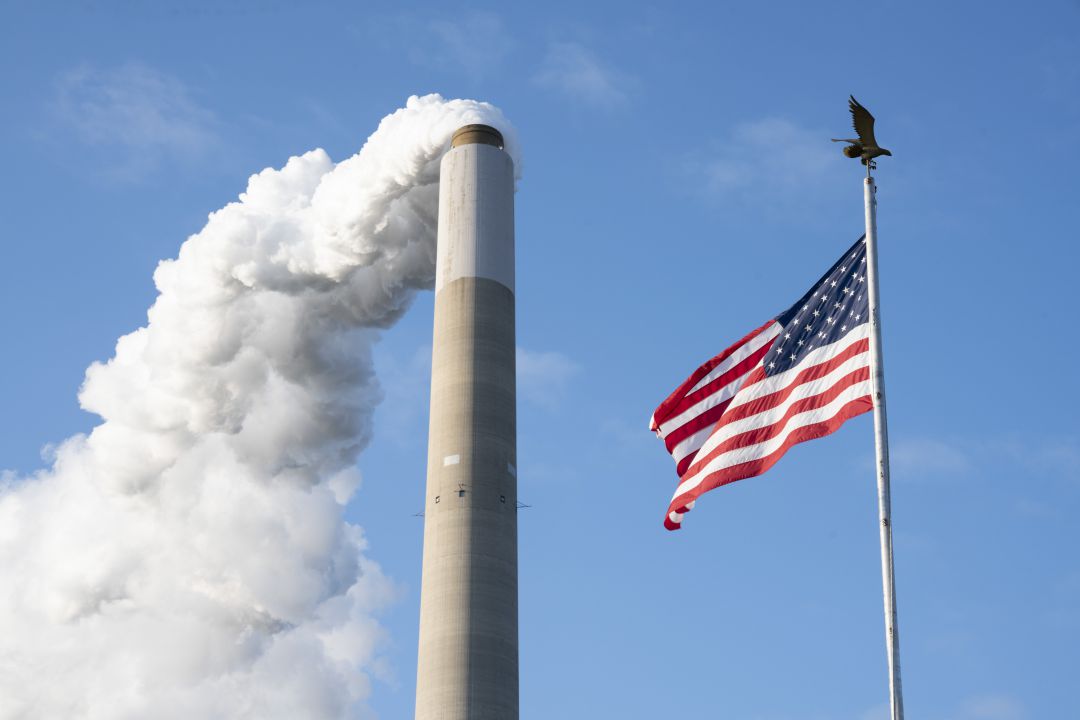 Las emisiones de gases de una chimenea junto a una bandera estadounidense. Las emisiones de gases de una chimenea junto a una bandera estadounidense.