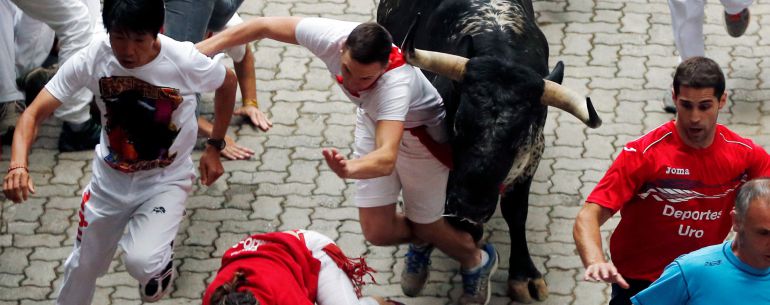 Varios jóvenes corren el sexto encierro de San Fermín mientras uno de ellos es cogido por un toro