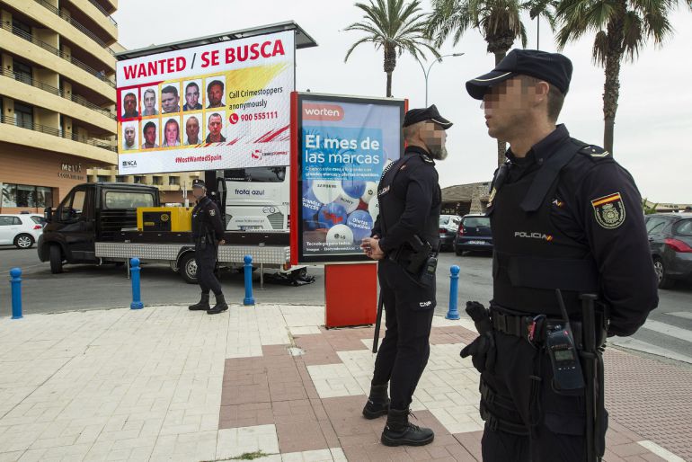 Agentes de la Policía Nacional frente a una pantalla donde figuran las fotografías de los 10 fugitivos más buscados por las autoridades británicas