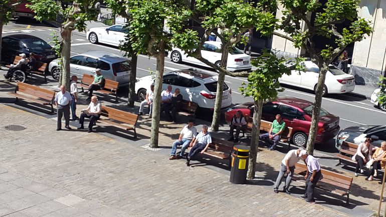 Varias personas sentadas al sol en la plaza de Unzaga de Eibar