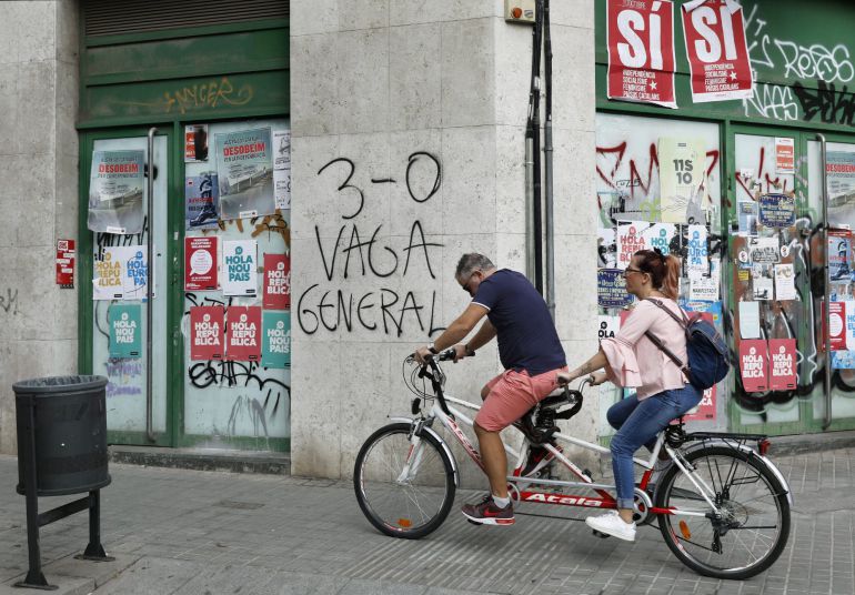 Varias personas pasan ante una pintada en el barrio de Sants de Barcelona, alusiva al paro general convocado para este martes
