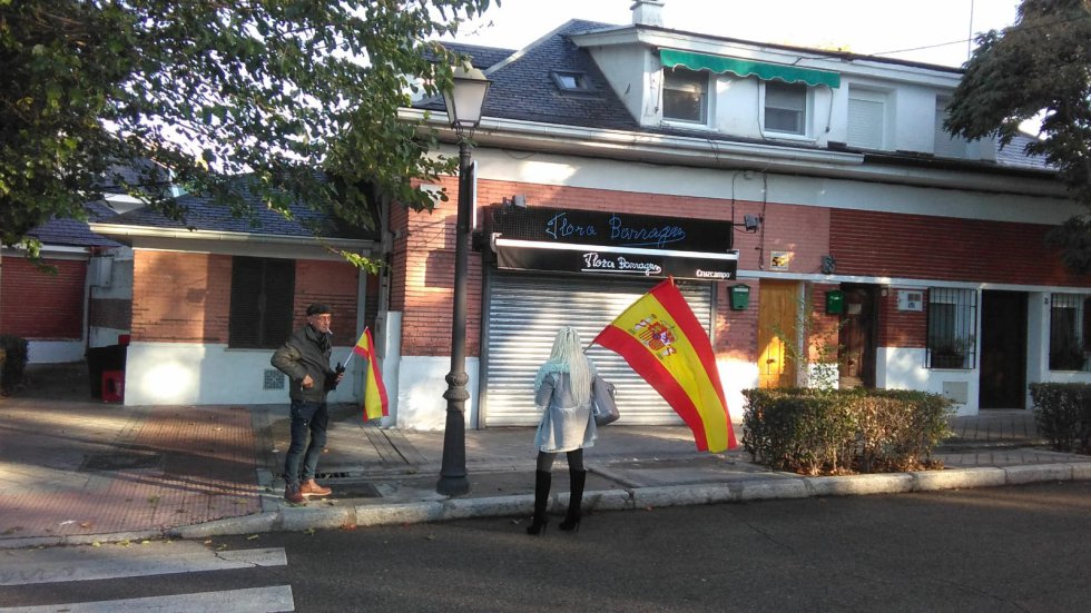 Una cafetería cerrada en Mingorrubio. Frente a él dos personas portando banderas de España Una cafetería cerrada en Mingorrubio. Frente a él dos personas portando banderas de España