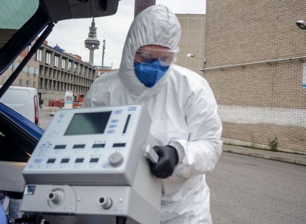 Un técnico protegido con un traje, guantes y mascarilla en el Hospital Gregorio Marañón, saca un respirador del maletero de su coche