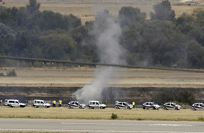 Varios coches de Policía apostados cerca del lugar de la tragedia, donde se vislumbran enormes columnas de humo