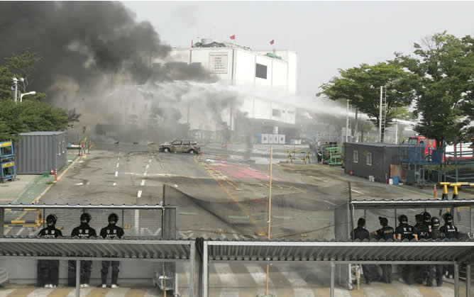 Los bomberos extinguen el fuego de los neumáticos encendidos por los huelguistas en el interior de la fábrica, mientras la Policía mira desde afuera.