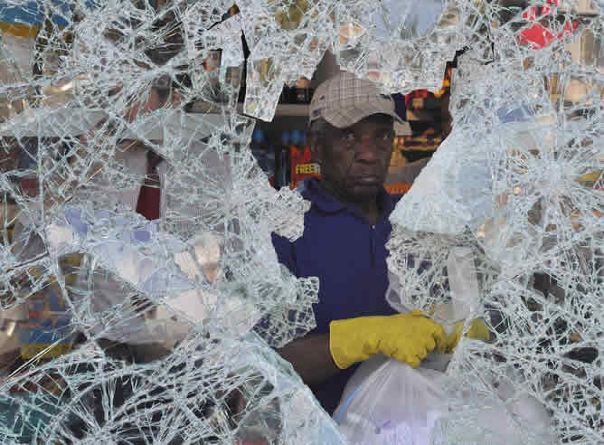 Un hombre recoge los restos de ventana de un supermercado arrasado por los disturbios de esta madrugada.