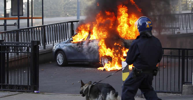 Un policía y su perro se dirigen hacia un coche en llamas en Birmingham, al centro de Inglaterra