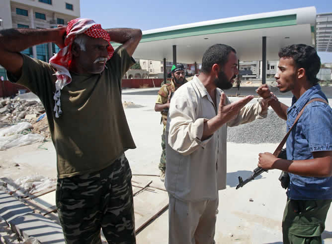 Un hombre discute con un rebelde que pretende arrestar a uno de sus trabajadores cerca de un control en Trípoli