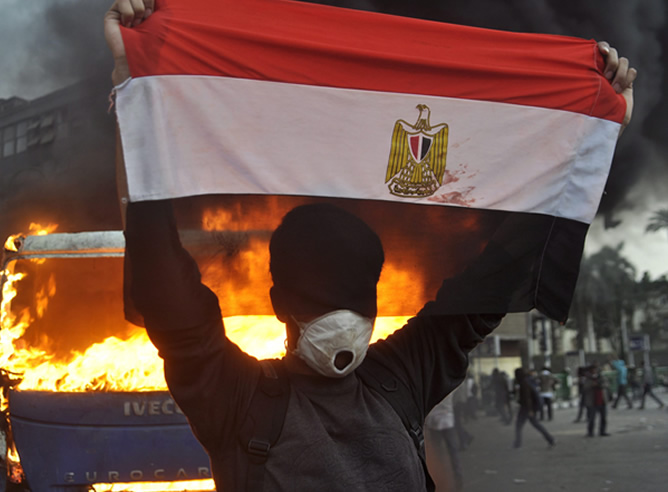 Un egipcio sujeta la bandera nacional frente a un coche de la policía que está en llamas en El Cairo