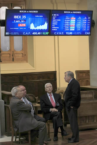 Cuatro inversores asiduos al palacio de la Bolsa de Madrid conversan bajo dos paneles informativos del parqué madrileño