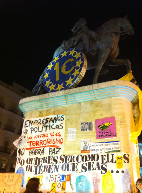 La estatua ecuestre de Carlos III es ya uno de los símbolos de las movilizaciones del 15-M, con una maqueta del euro y carteles a su alrededor con sus consignas.