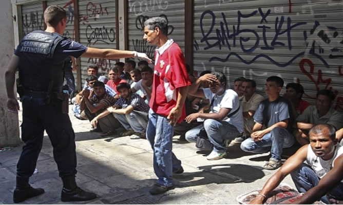 Un policía griego mantiene retenidos a unos inmigrantes residentes en Atenas
