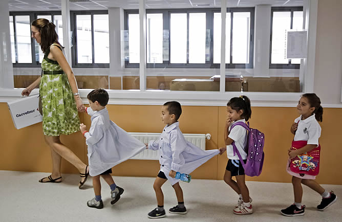 Un grupo de niños en fila se dirigen a clase con la profesora al inicio del curso escolar, en el colegio Leopoldo Calvo Sotelo en Madrid