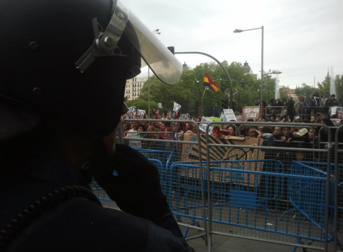 Los manifestantes gritan y esperan tras las vallas y frente a los policías que controlan el recorrido de la marcha del 25-S