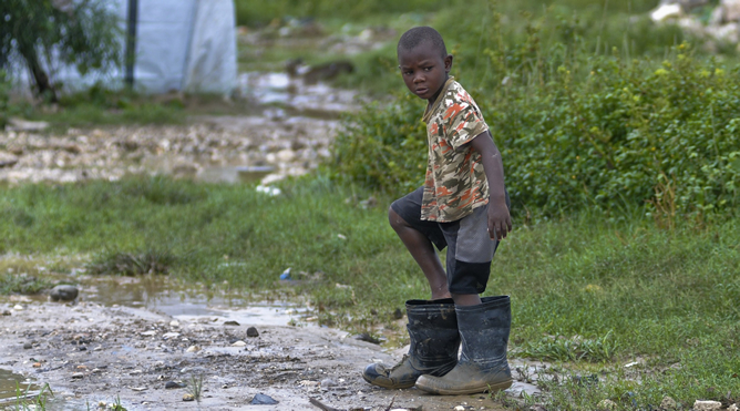 Un niño se pone unas grandes botas de agua tras el paso del huracán 'Sandy' por Haití