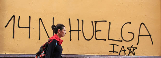 Una joven camina por una calle de Sevilla en la que se ve una pintada de la huelga general