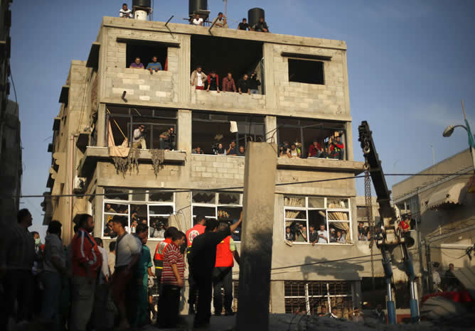 Un grupo de palestinos se reúnen alrededor de una casa destruida como miembros de la defensa civil para buscar víctimas bajo los escombros después de un ataque aéreo israelí en Gaza.