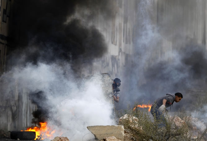 Palestinos a cubierto de gas lacrimógeno lanzado por las fuerzas de seguridad israelíes durante los enfrentamientos cerca de Ramallah. REUTERS/Ammar Awad