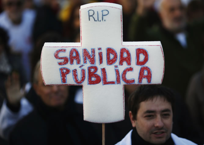Un manifestante con una cruz que se lee 'RIP cuidado, la salud pública' durante la tercera 'marea blanca'.