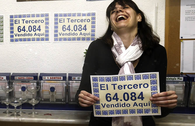 La propietaria de la administración de Alcalá de Henares que ha vendido el tercer premio de la Lotería de Navidad muestra el número agraciado, el 64.084, en el interior del establecimiento.