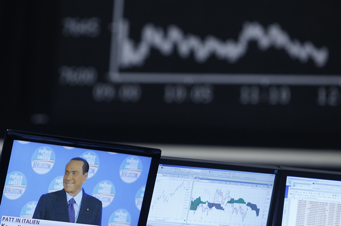 Imagen de Silvio Berlusconi en una pantalla de televisión y al fondo la cotización del DAX alemán