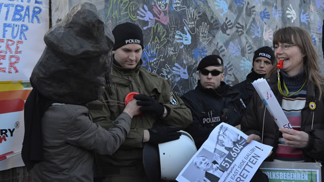 Un participante en la manifestación junto al muro de Berlín ausculta a un policía.
