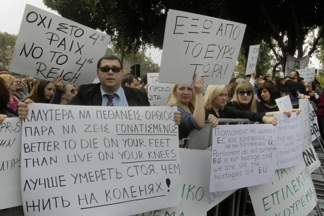 Los manifestantes que han protestado ante el parlamento de Chipre portaban pancartas con mensajes en contra del rescate