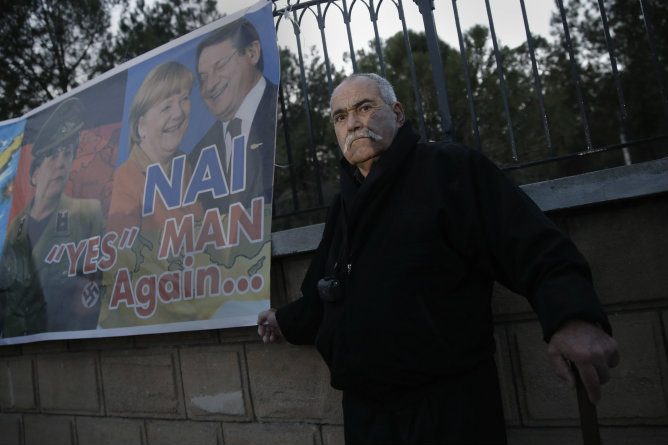 Un manifestante se encuentra junto a una bandra en la que aparecen Angela Merkel y Nicos Anastasiades durante una manifestación contra el rescate en Nicosia