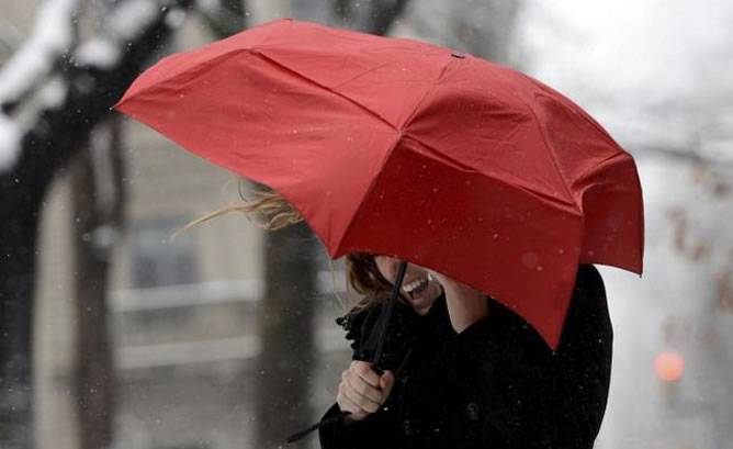 Una mujer habla por su teléfono móvil tratando de protegerse del viento y de la lluvia con un paraguas