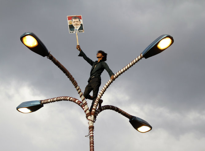 Un partidario del depuesto presidente egipcio Mohamed Mursi sostiene su foto mientras está de pie en la parte superior de un poste de luz