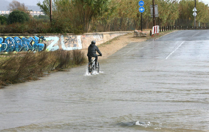Un hombre pasea en bicicleta por el barrio marítimo de El Vendrell (Tarragona), una de las zonas de Cataluña que está sufriendo el fuerte temporal de lluvia y viento