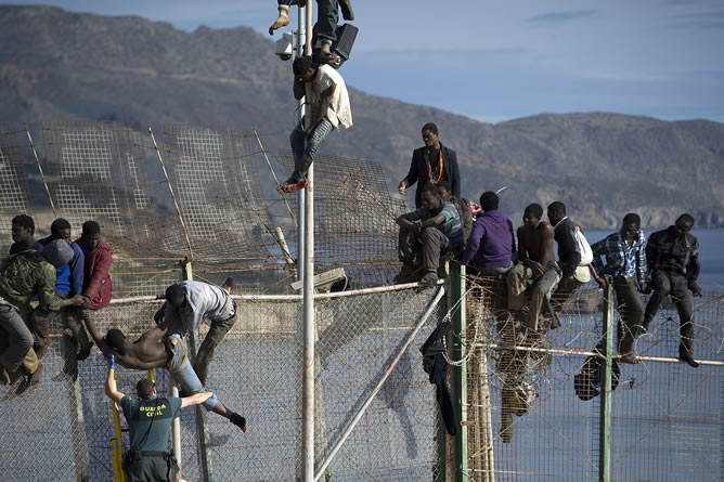 Un agente de la Guardia Civil ayuda a uno de los 25 inmigrantes de origen subsahariano que permanecen encaramados en la parte alta de la valla de Melilla