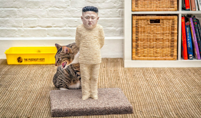 Un gato en un rascador de uñas con la figura de Kin Jong-un