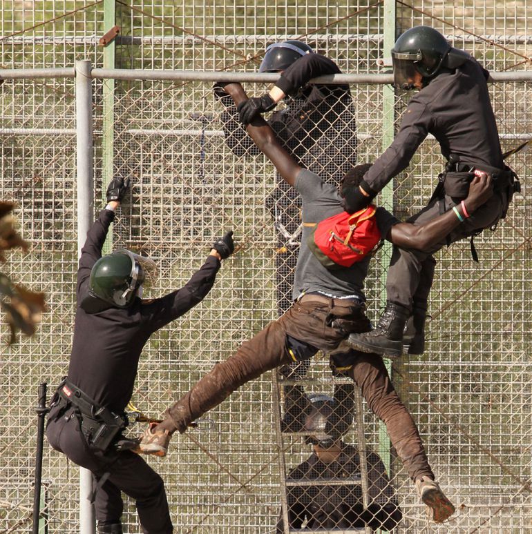 (22-10-14). Agentes de la policía vajan de la valla de Melilla a un grupo de inmigrantes. © Antonio Ruiz