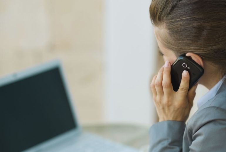 Una mujer realiza una llamada telefónica frente a un ordenador portátil