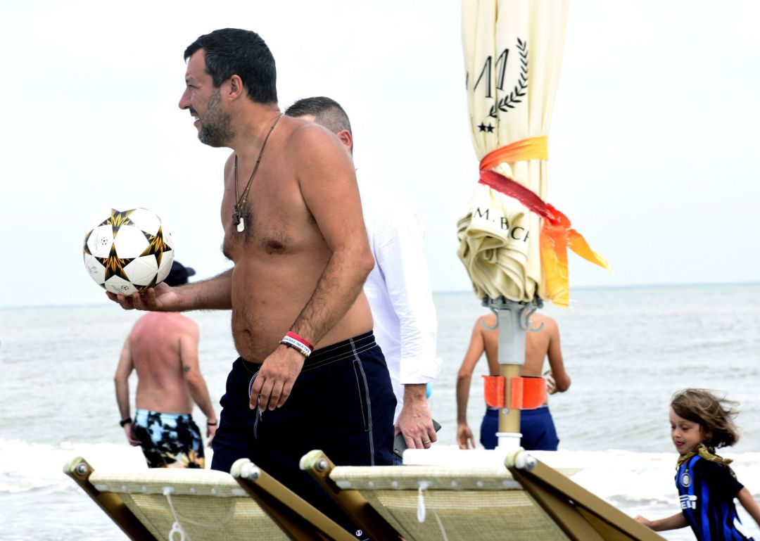 El ministro del Interior italiano, Matteo Salvini, camina con un balón de fútbol en la mano en la playa en que su hijo ha subido a dar un paseo a una moto de agua de la Policía.