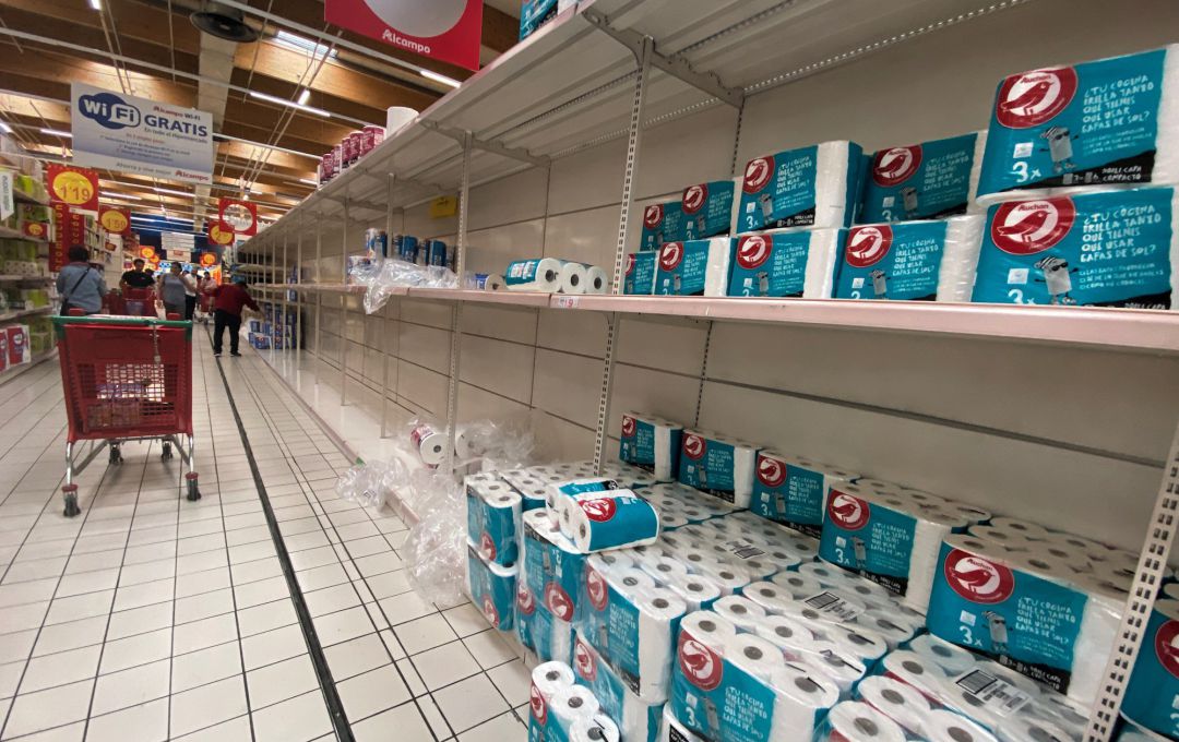 Estanterías con ausencia de productos y otras con papel higiénico y papel de cocina en un supermercado 