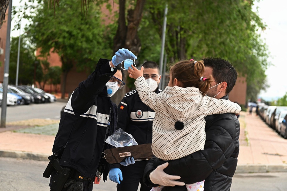 Una agente de la policía entrega una mascarilla a una niña que pasea en brazos de su padre. Una agente de la policía entrega una mascarilla a una niña que pasea en brazos de su padre.