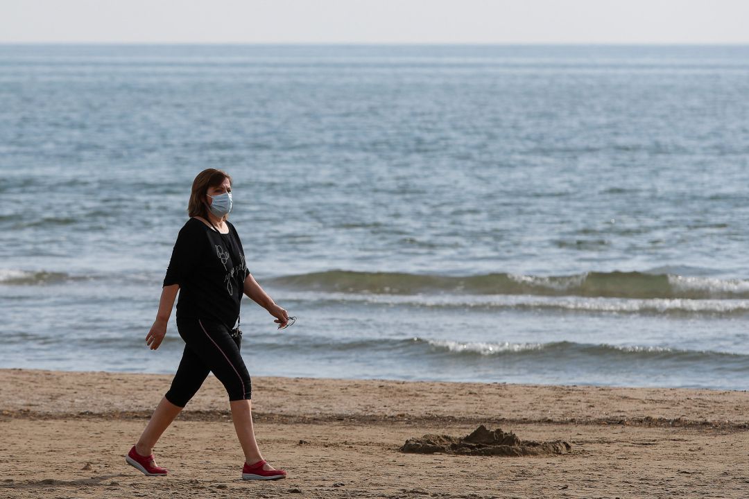 Una mujer con mascarilla pasea por la playa de la Malvarrosa 