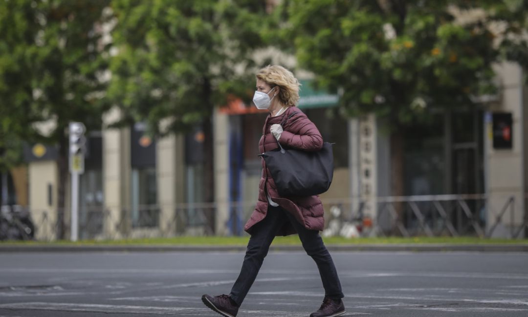 Una mujer caminando protegida con mascarilla y guantes.