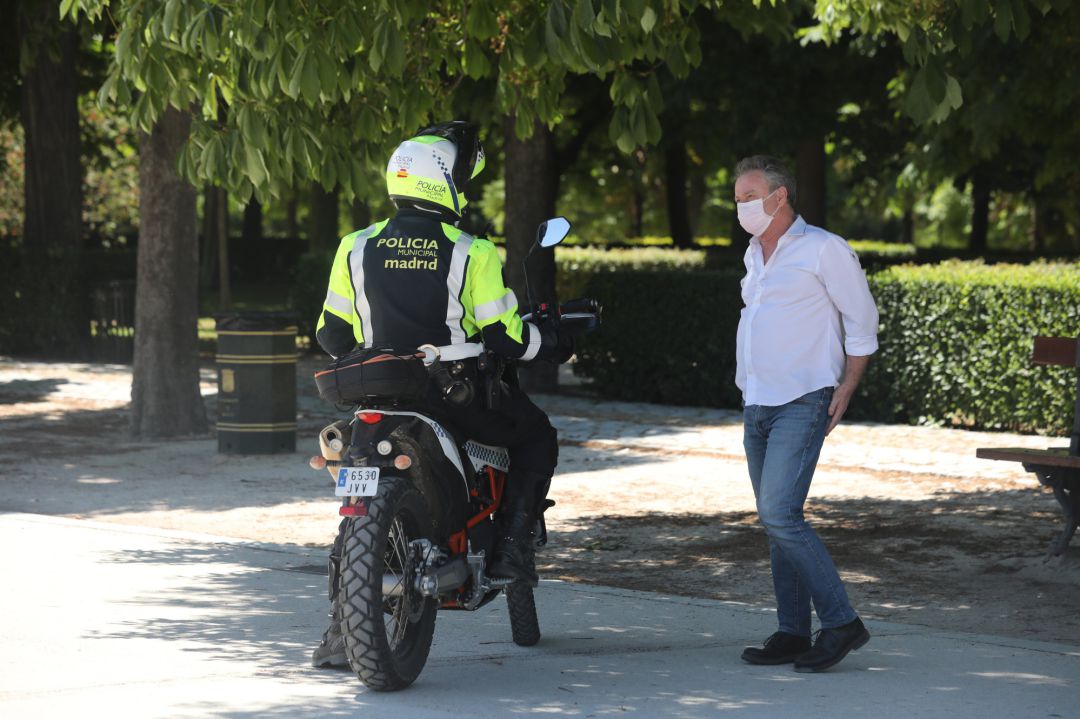 Un policía municipal habla con un transeúnte que camina por el Parque de El Retiro en Madrid.