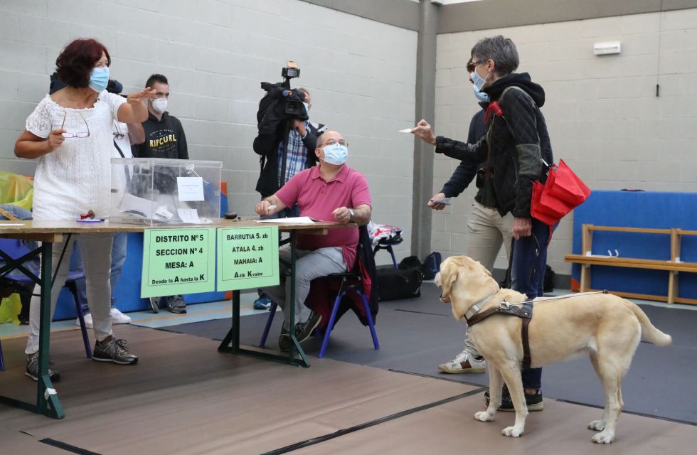 Una mujer invidente acompañada de su perro en el momento de votar en un colegio electoral en la localidad vizcaína de Durango, muestra su carnet de identidad guardando la distancia de seguridad. Una mujer invidente acompañada de su perro en el momento de votar en un colegio electoral en la localidad vizcaína de Durango, muestra su carnet de identidad guardando la distancia de seguridad.