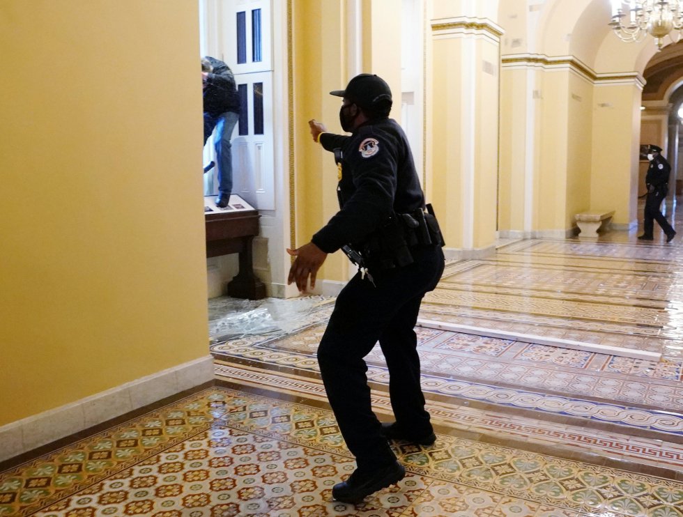 Un policía advierte a los seguidores de Trump para que no sigan avanzando en el interior del Capitolio. Un policía advierte a los seguidores de Trump para que no sigan avanzando en el interior del Capitolio.