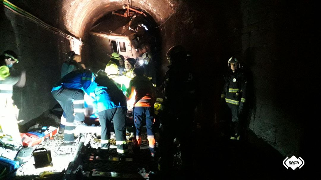 Personal sanitario atiende al maquinista herido con, al fondo, la locomotora del tren atravesada en la boca del túnel. 