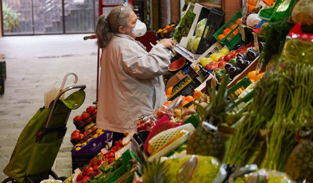 Una señora con mascarilla comprando en un mercado.