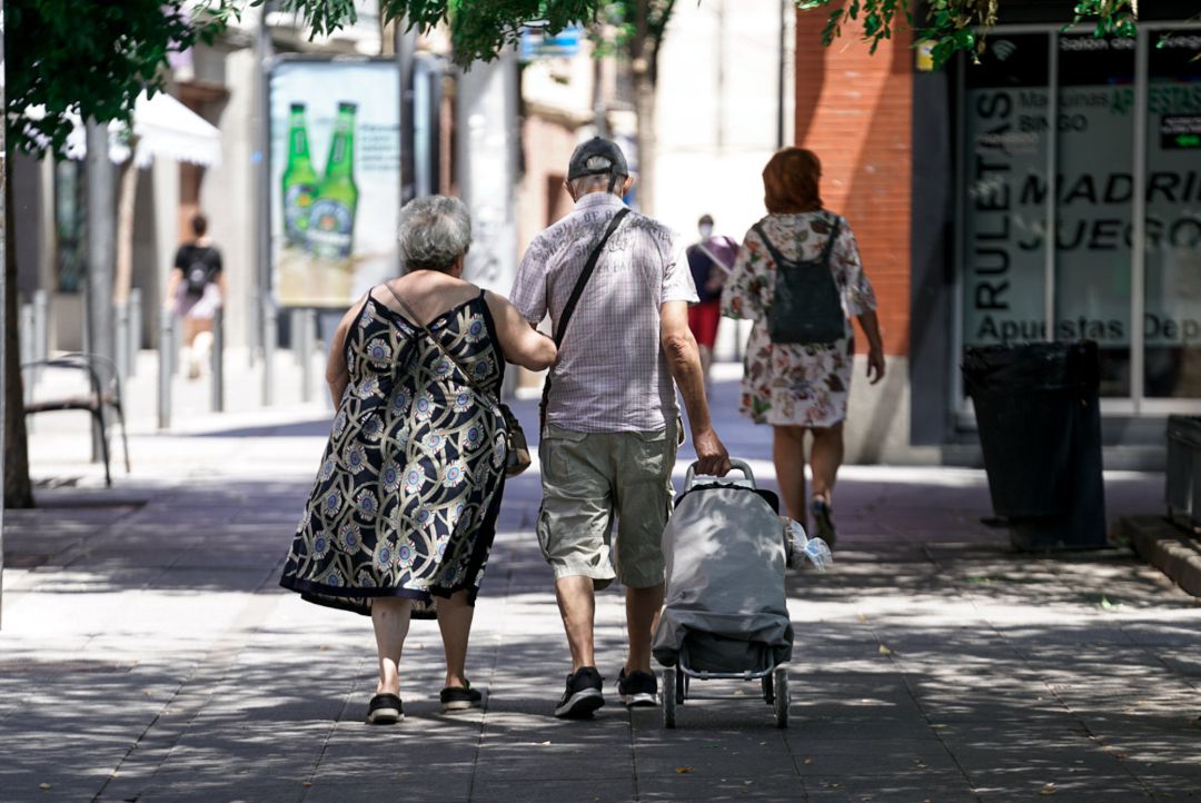 Una pareja de ancianos camina por la calle con un carro de compra el pasado verano